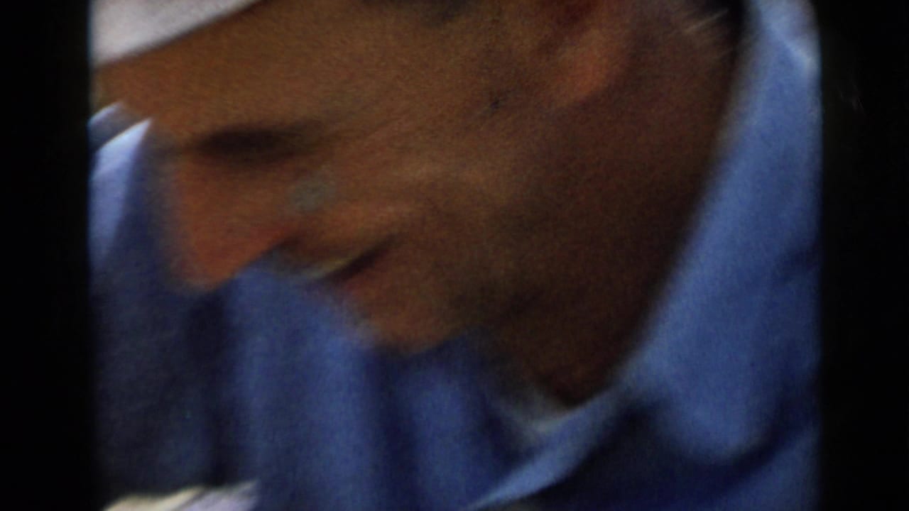 1949 San Diego home-movie frame showing an adult man in a blue shirt leaning downward, partly blurred by handheld 8mm motion.