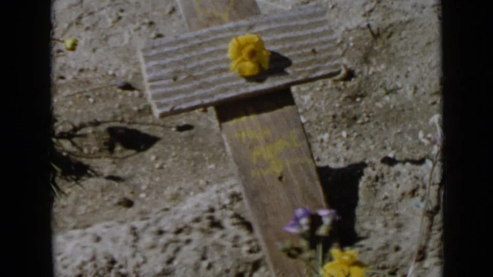 Close home-movie view of a small flower-adorned wooden cross in a dry San Diego-area landscape, matching the 1949 clip metadata.