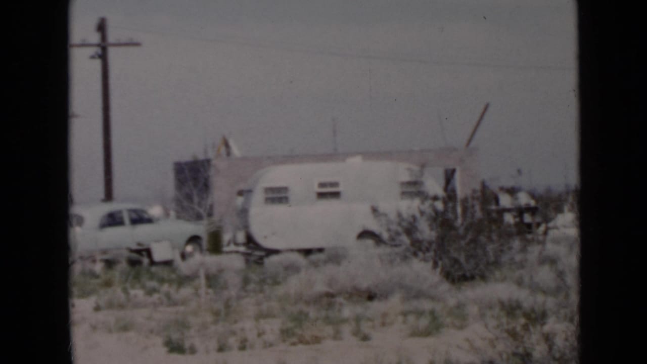 San Diego-area 1949 home-movie frame showing a travel trailer, parked car, utility pole, and sparse residential ground.