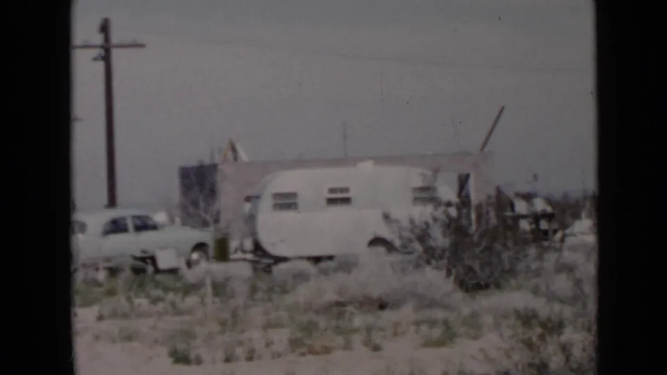 San Diego-area 1949 home-movie frame showing a travel trailer, parked car, utility pole, and sparse residential ground.
