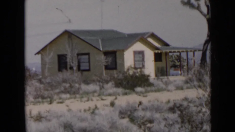 1949 San Diego-area home-movie frame showing a small yellow ranch-style house set among dry shrubs under a hazy sky.