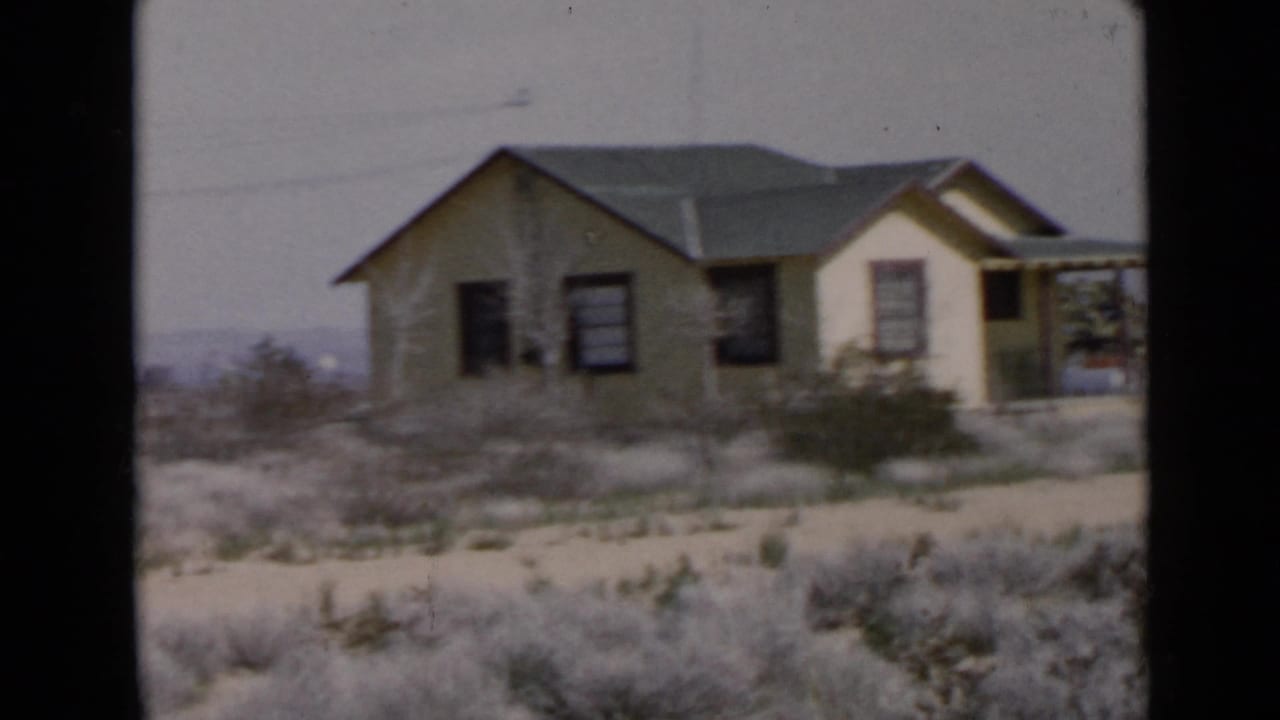 Small house seen from farther back across dry brush and sandy ground.