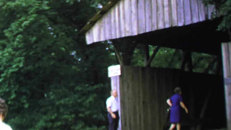 1969 Washington DC footage frame with a woman entering the shadowed covered bridge and a man visible near the left post.