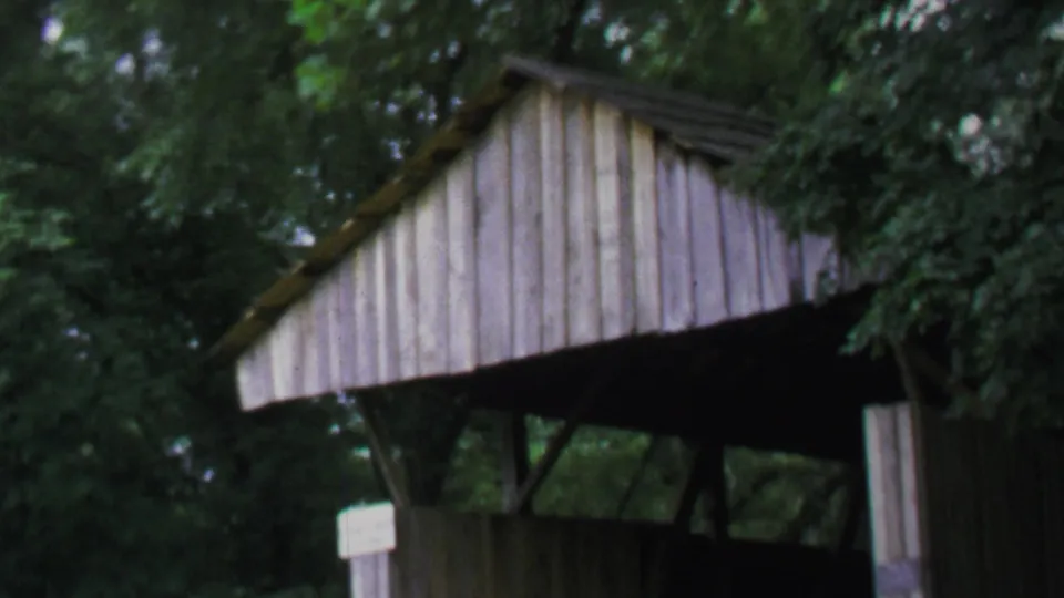 Final 1969 Washington DC frame holds on the covered bridge facade, leafy branches, shadowed interior, and posted sign.