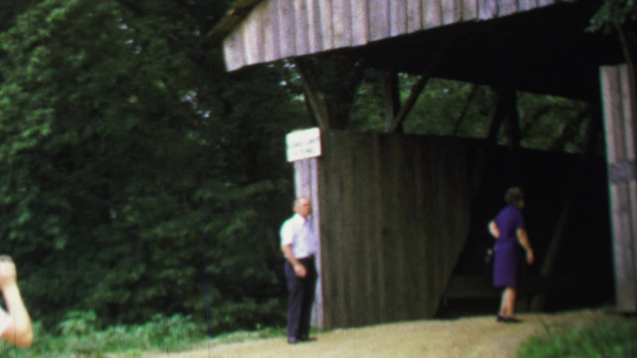 Man and woman at the entrance of a wooden covered bridge.