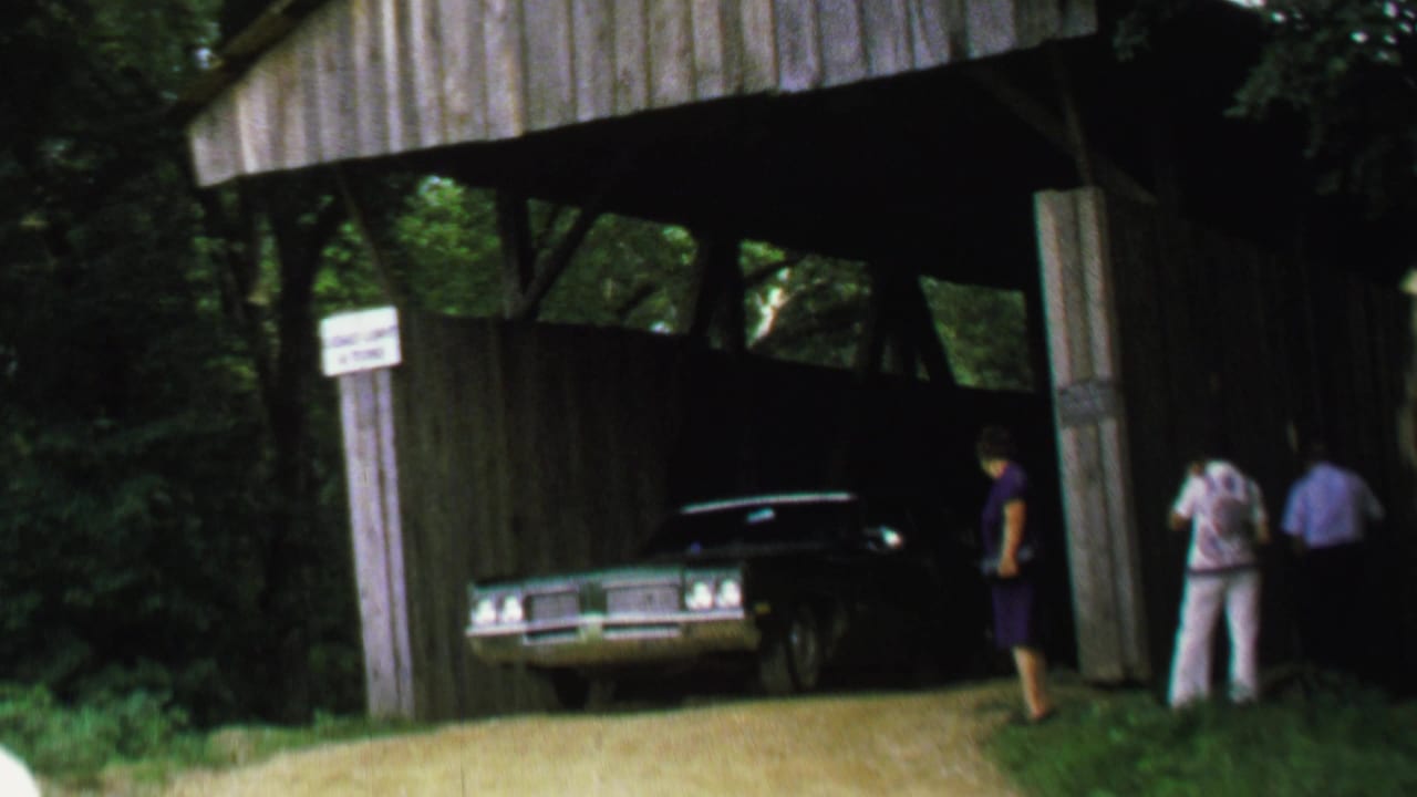 Sedan under the covered bridge with bystanders near the right side of the entrance.