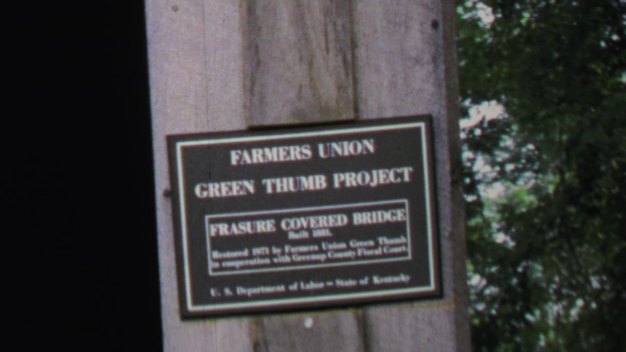 Posted Green Thumb Project sign beside a wooded dirt road and parked cars.