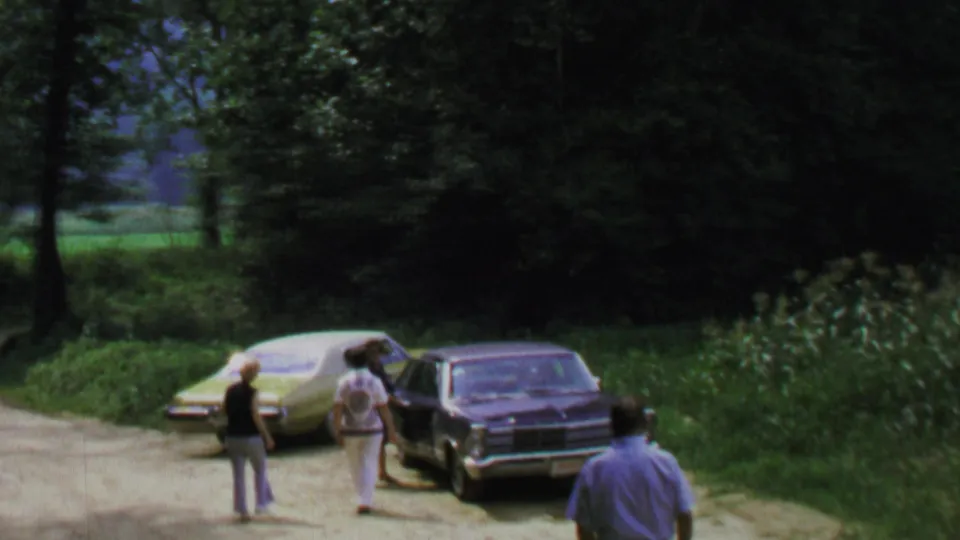 Final frame shows adults near light and dark sedans on a shaded dirt road, with a partial foreground person at right.