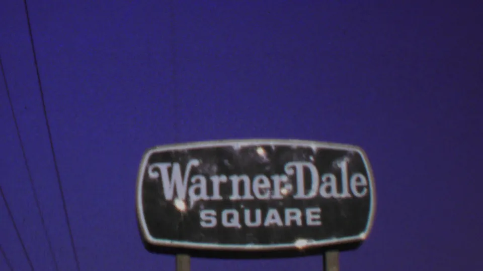 1969 Washington, DC-area frame of a weathered Warner-Dale Square sign on posts, filmed against blue sky with utility wires nearby.