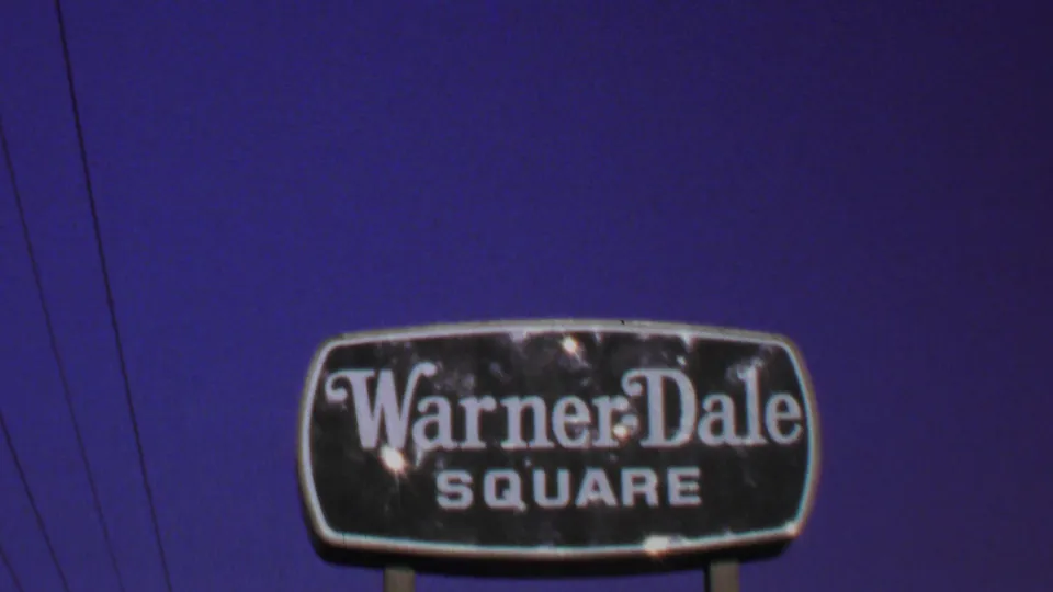 Close view of the Warner-Dale Square sign in 1969 Washington, DC-area 8mm footage, with blue sky and thin overhead wires visible.
