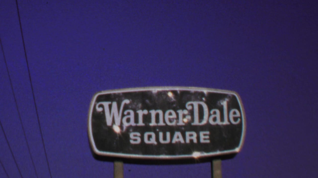 1969 Washington, DC home-movie frame showing the Warner Dale Square sign, utility wires, and deep purple-blue sky.
