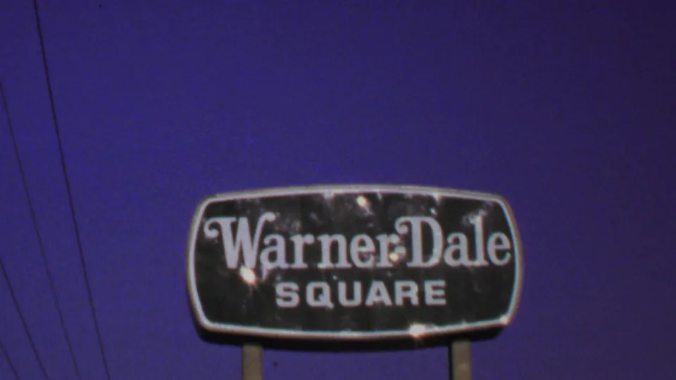 1969 Washington, DC home-movie frame showing the Warner Dale Square sign, utility wires, and deep purple-blue sky.