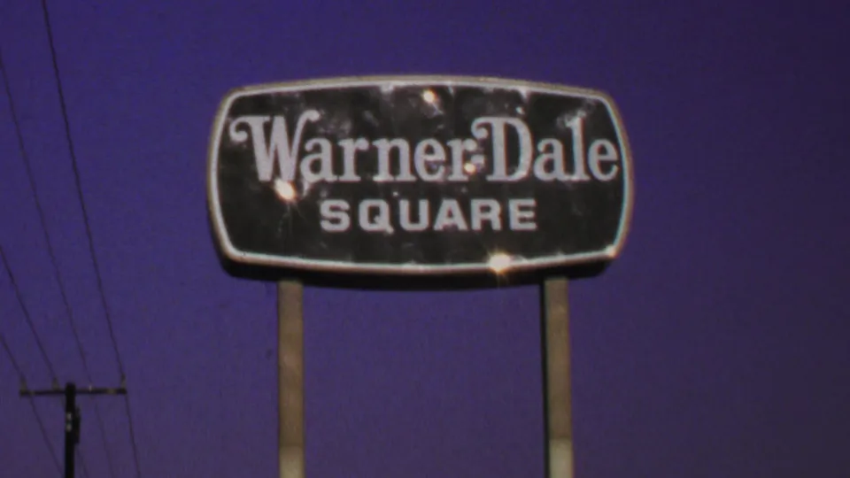 1969 Washington, DC home-movie still showing the Warner Dale Square sign with posts, wires, and film grain.