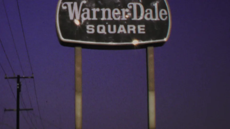 1969 Washington, DC home-movie frame showing a lit Warner-Dale Square roadside sign above power lines at night.