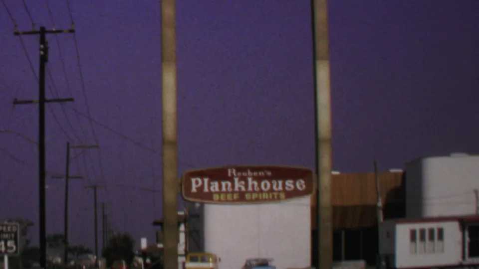 1969 Washington, DC frame showing the Reuben's Plankhouse sign, a roadside building, utility poles, and a small road sign at night.