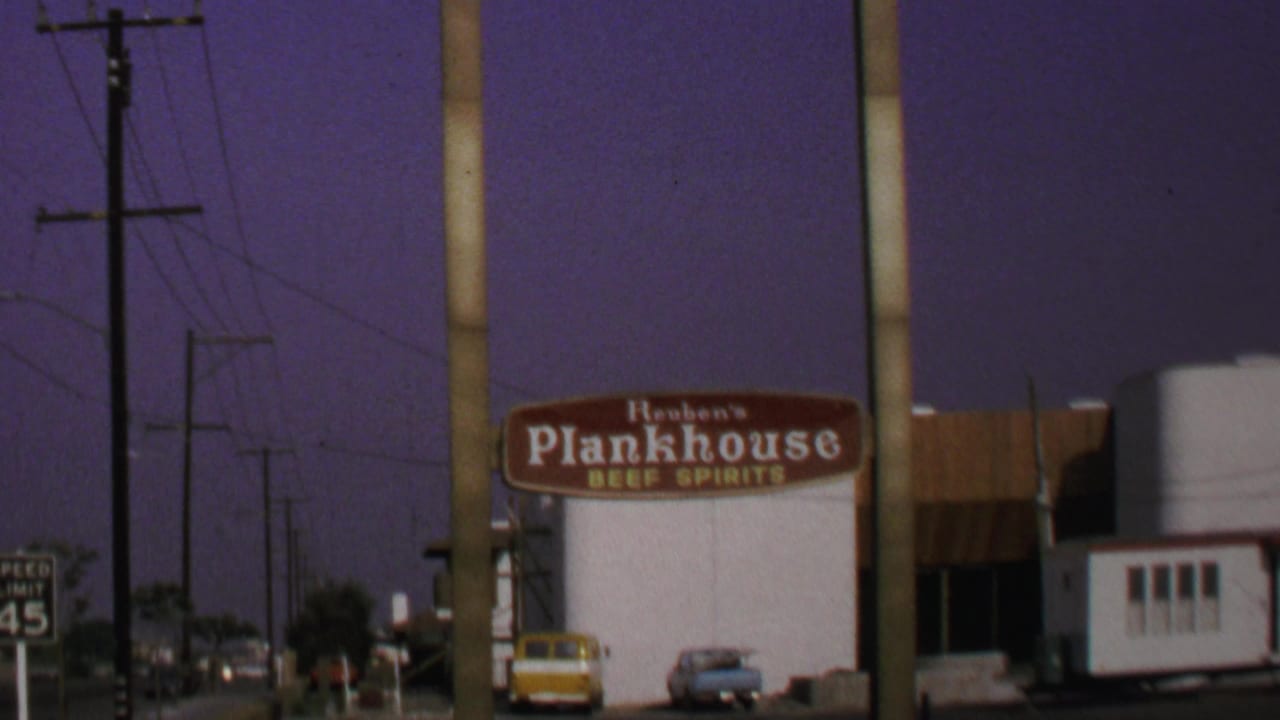 1969 Washington, DC 8mm frame showing the Reuben's Plankhouse sign, a low white building, parked cars, utility poles, and wires.