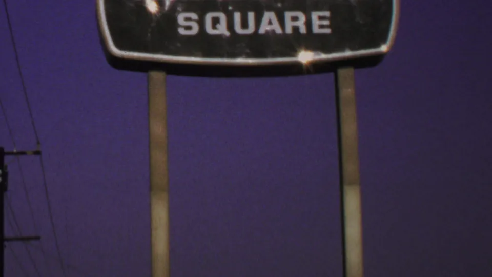 1969 Washington-area 8mm frame with a cropped Warner-Dale Square sign, tall supports, utility lines, and purple sky.