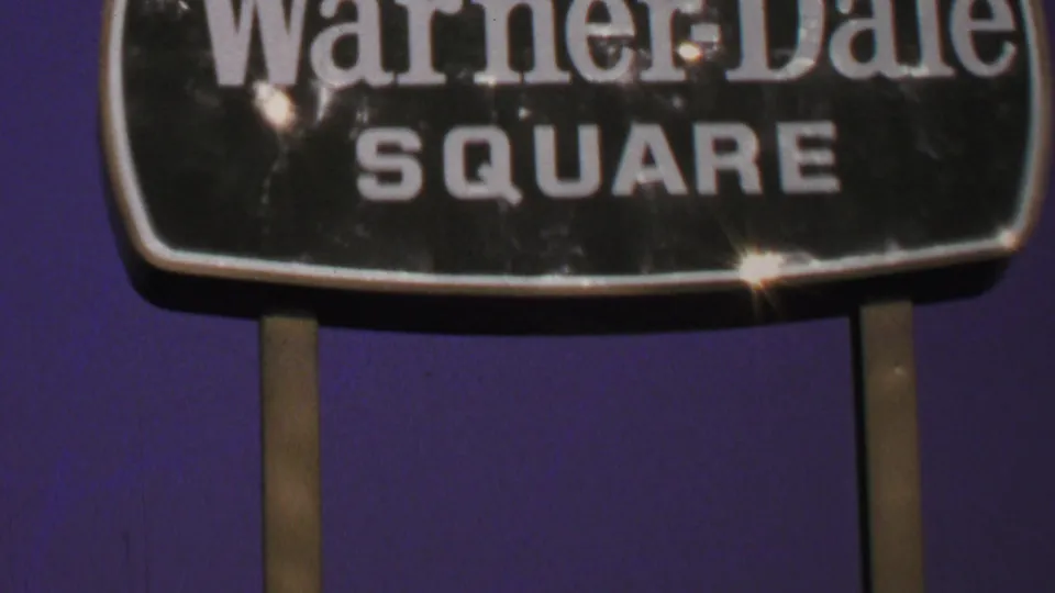 Close 1969 Washington-area frame of the Warner-Dale Square sign with visible lens flare, signposts, and 8mm grain.