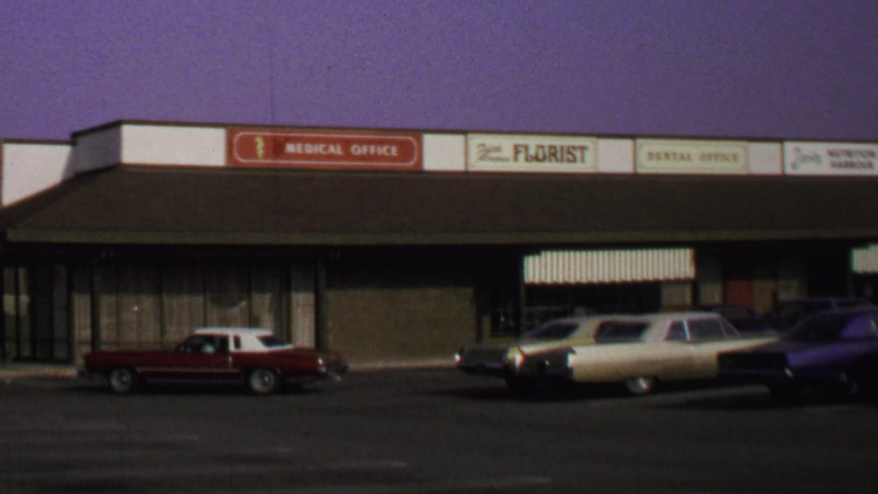 1969 Washington, DC frame of a low commercial strip with medical, florist, and dental signs above parked late-1960s cars.