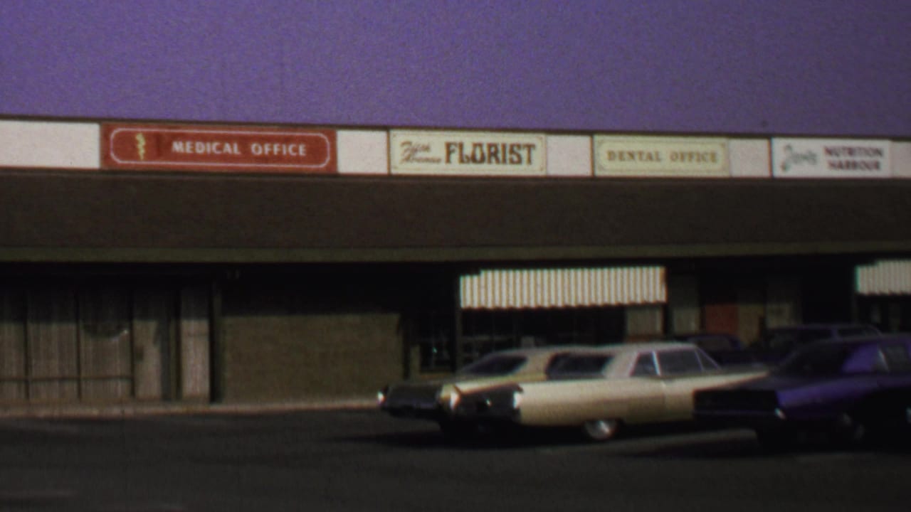 1969 Washington DC storefront row with medical office, florist, and dental office signs above parked period cars.