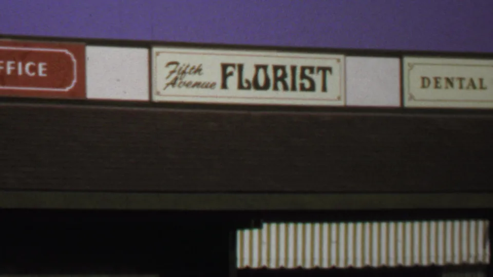 1969 Washington, DC home-movie frame showing a close zoomed view of a Fifth Avenue Florist sign beside dental and office signs.