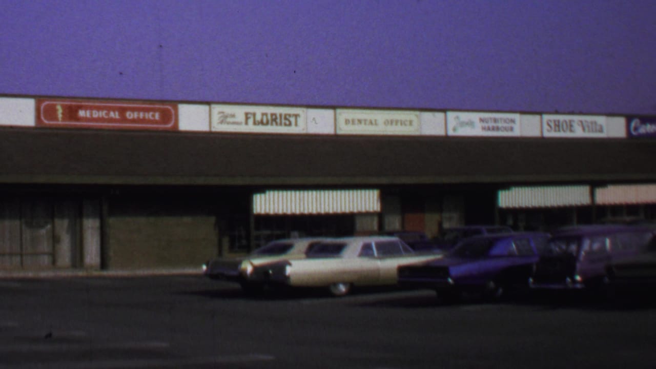 1969 Washington DC 8mm frame showing a shopping-center strip with storefront signage and parked period cars.