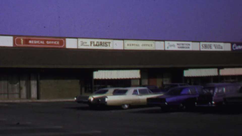 1969 Washington DC 8mm frame showing a shopping-center strip with storefront signage and parked period cars.