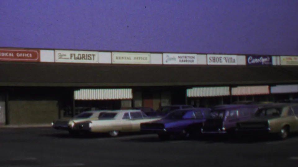 1969 Washington DC frame showing a retail strip, visible shop names, and several parked 1960s cars.