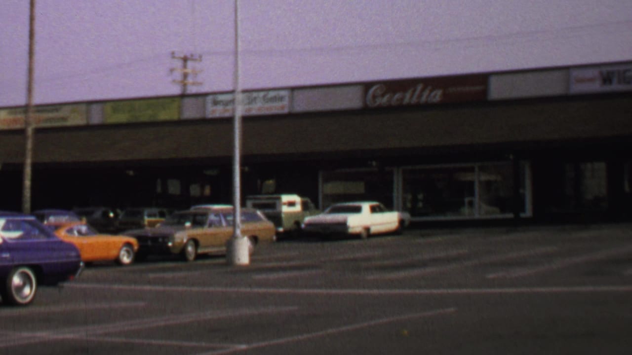1969 Washington, DC shopping-center view with parked late-1960s cars, storefront signage, and a broad asphalt lot.