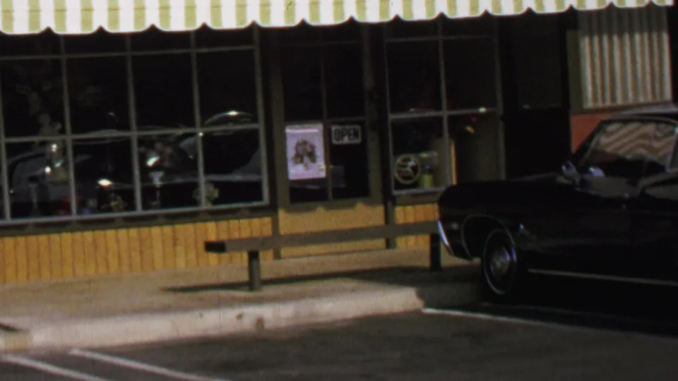 Final frame of the 1969 Washington, DC storefront shows the dark car, reflective panes, open sign, bench, and striped awning.