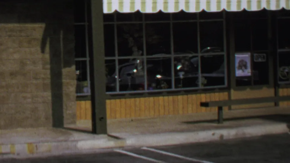 1969 Washington, DC storefront facade with striped awning, large windows, a bench, curb, and empty parking lines visible in front.
