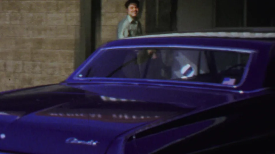 1969 Washington, DC street view with a man near the storefront and a dark blue classic car passing or parked across the foreground.