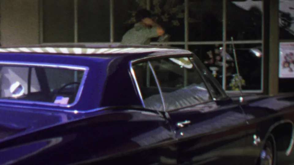 1969 Washington, DC frame of a glossy blue classic car in the foreground, storefront windows behind it, and a man near the window display.