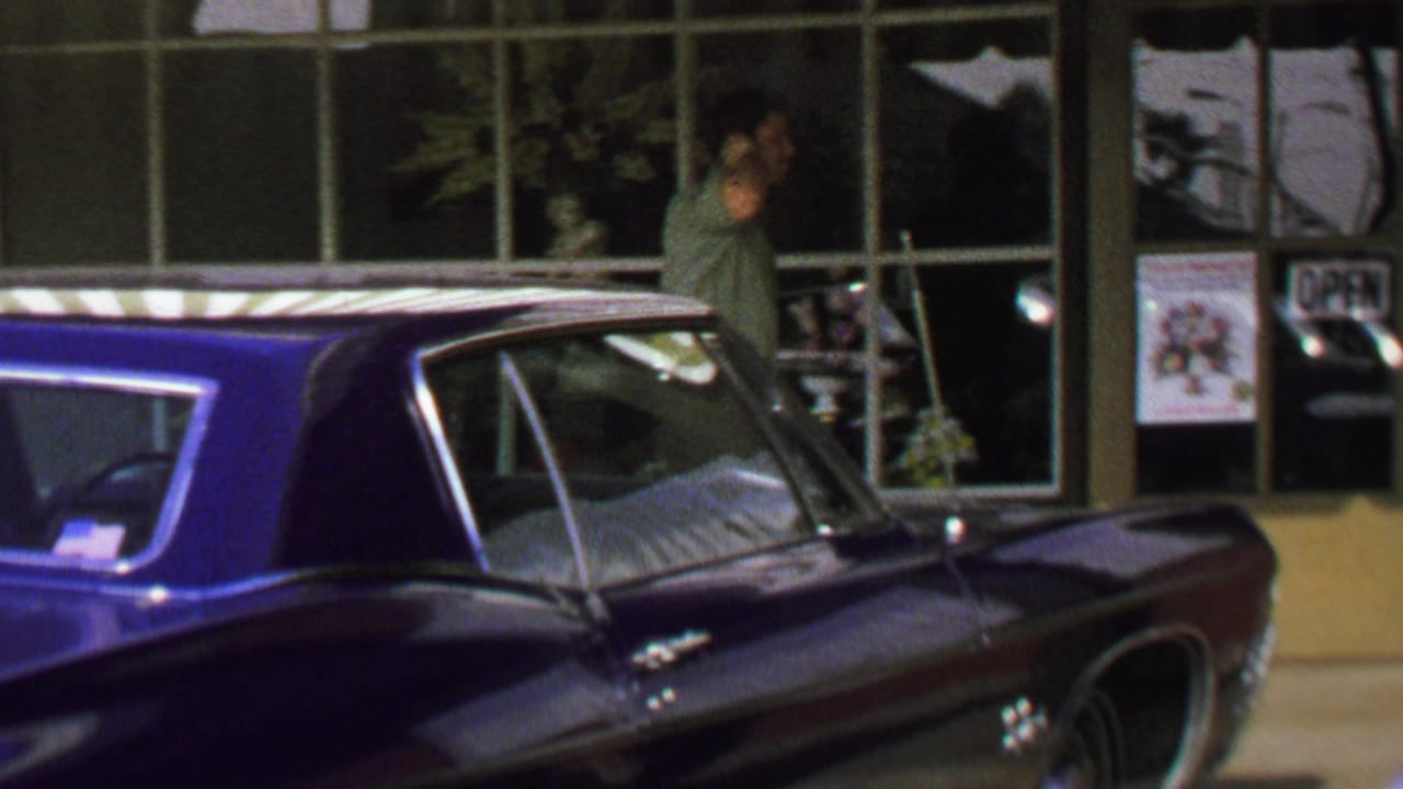 1969 Washington, DC home-movie frame showing a man near large storefront windows behind a dark classic American car.