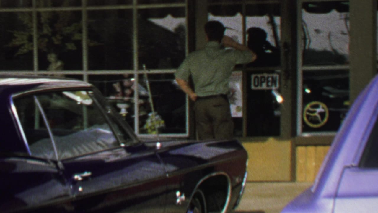Man faces a storefront door near an OPEN sign while a dark car is parked in front.