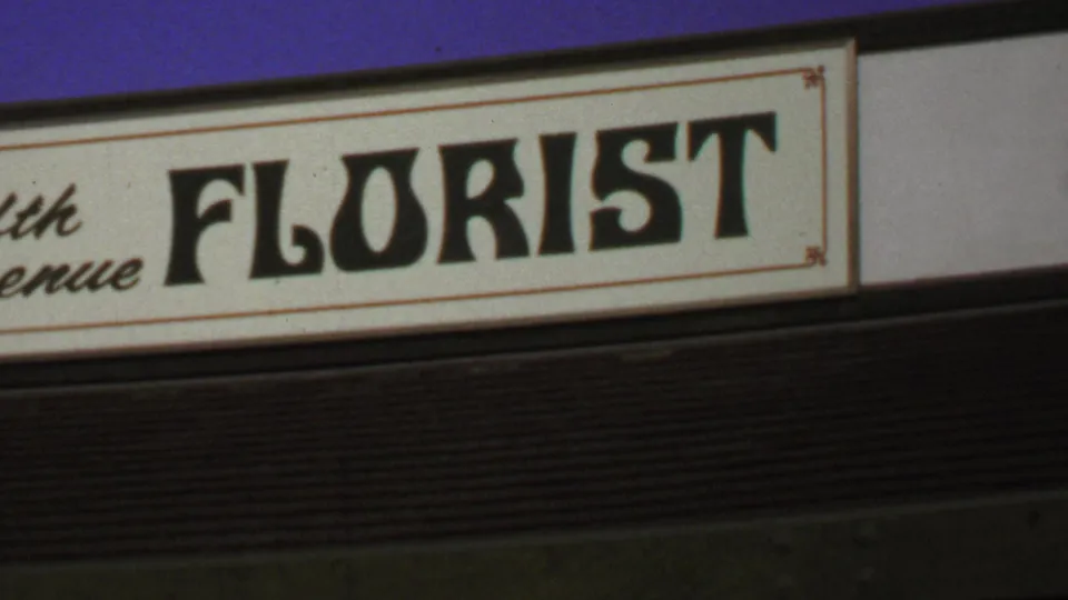 The camera frames the Fifth Avenue Florist sign in Washington, DC, with cream background, black lettering, and blue fascia above.