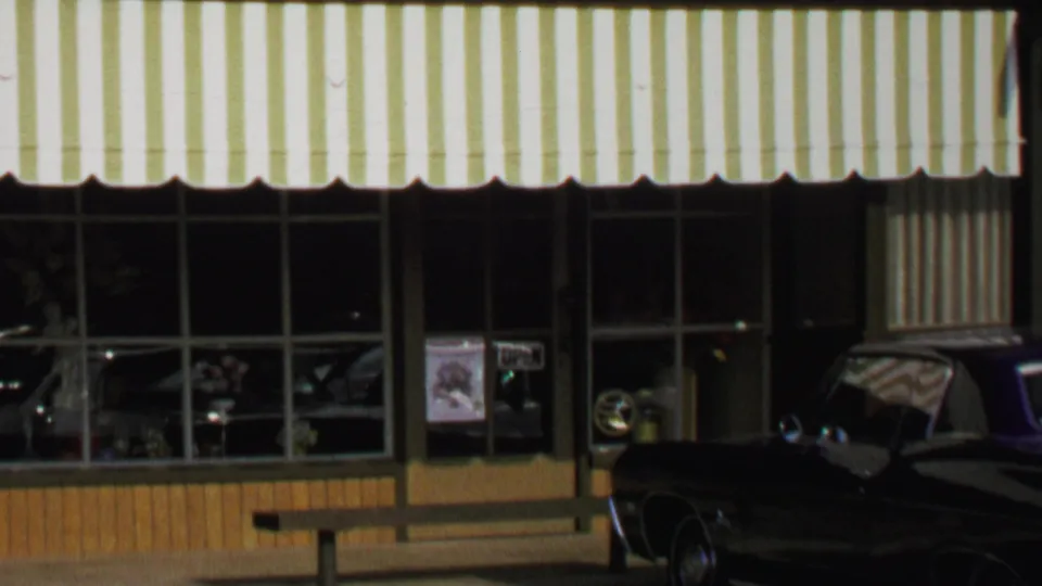 1969 Washington, DC home-movie view of the florist exterior with striped awning, display windows, and a dark classic car parked outside.