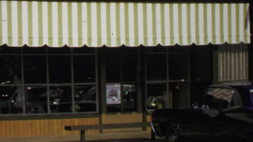 1969 Washington, DC frame showing the florist storefront under a yellow and white awning with window displays and a parked dark car.