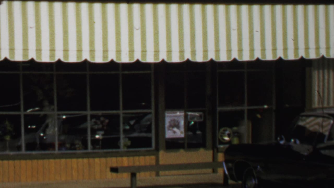 Storefront windows beneath a green-and-white striped awning with a dark car parked at the curb.