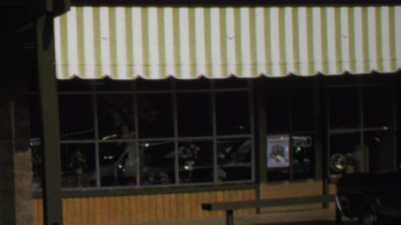 A Washington, DC storefront in 1969 shows a striped awning, large window bays, poster in the glass, and a car at the right edge.