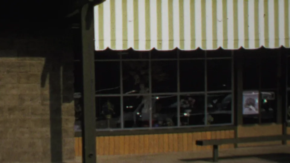 Closer 1969 Washington, DC storefront view with awning, display windows, bench, poster, and cars reflected in the glass.