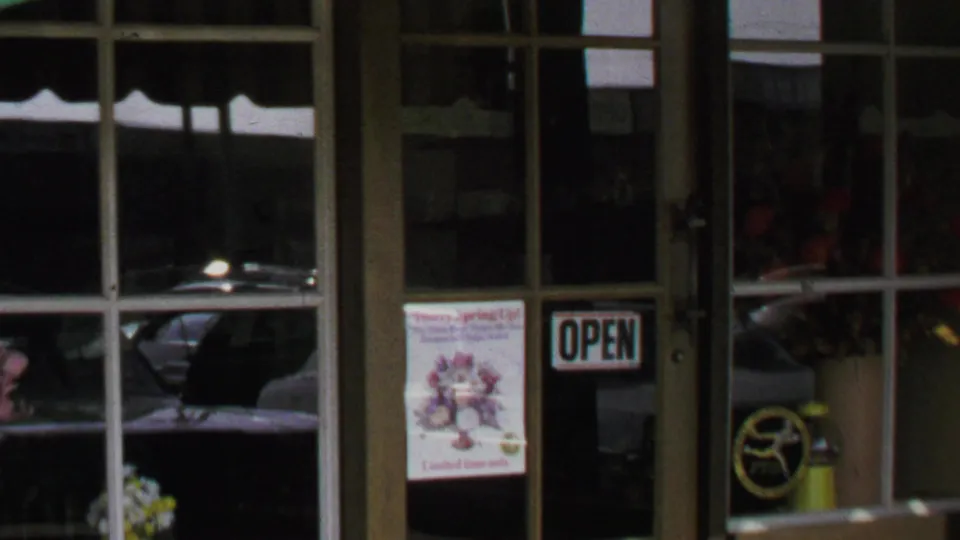 Close 1969 Washington, DC storefront detail showing the OPEN sign, spring event poster, glass door, awning edge, and reflected car.