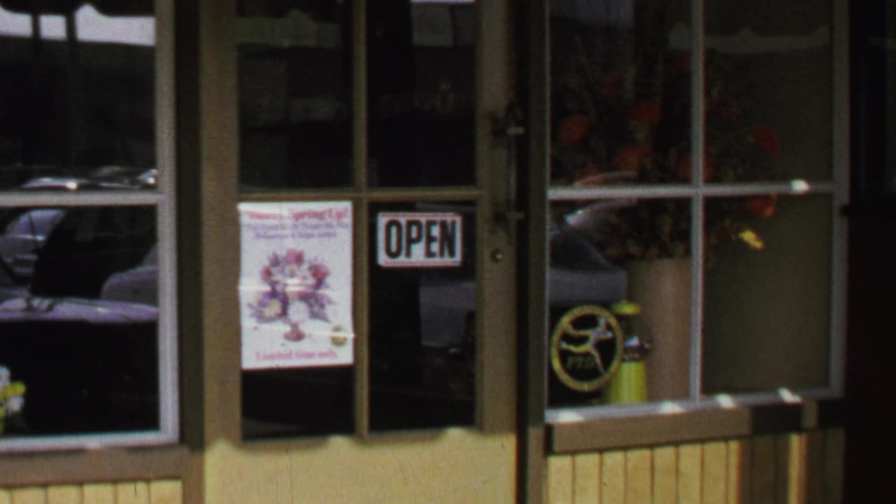 1969 Washington, DC shop entrance with an open sign, flower poster, dark window reflections, and a yellow extinguisher-like cylinder.