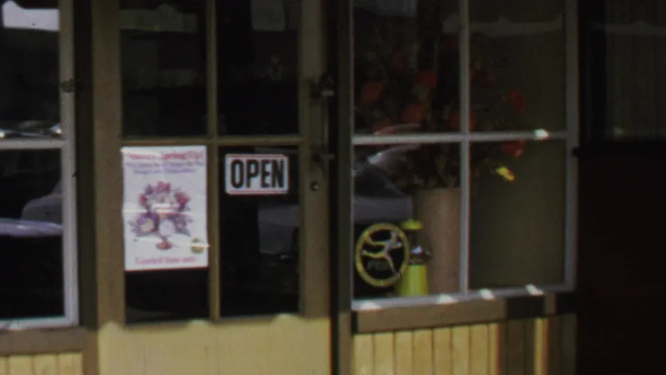 1969 Washington, DC storefront close view showing an open sign, flower poster, reflected cars, and interior shop objects.