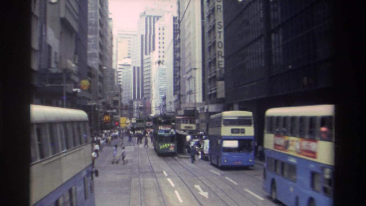 Double-decker buses and a green tram on a busy urban street lined with tall buildings.