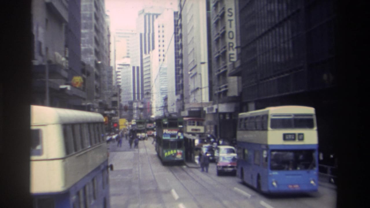 Blue-and-cream double-decker buses pass cars and pedestrians on a dense city street.