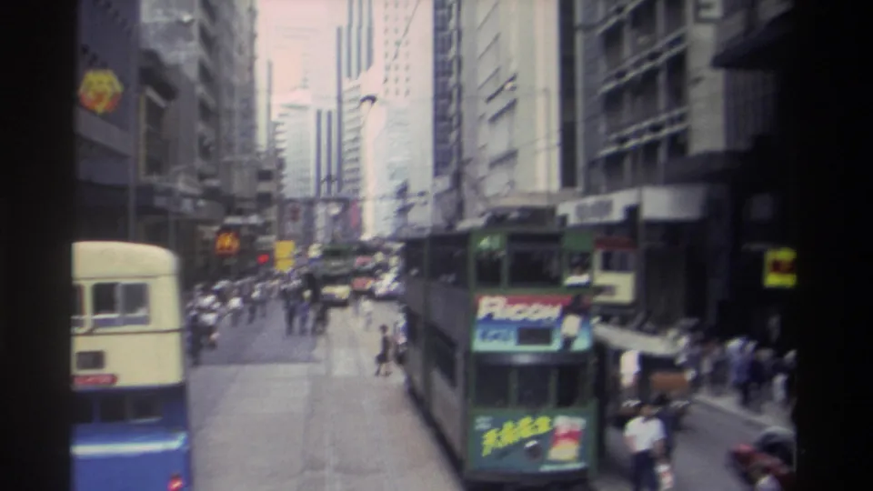 1982 Hong Kong traffic scene with a green tram, pedestrians, cars, tall buildings, and visible Ricoh and McDonald's signage.