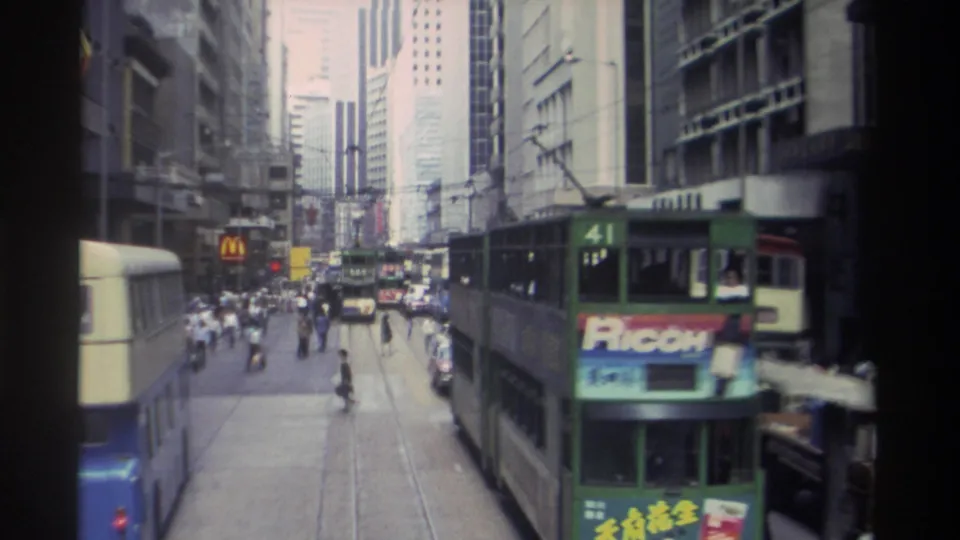 1982 Hong Kong street frame showing a route 41 green tram with Ricoh advertising, a double-decker bus, pedestrians, and traffic.