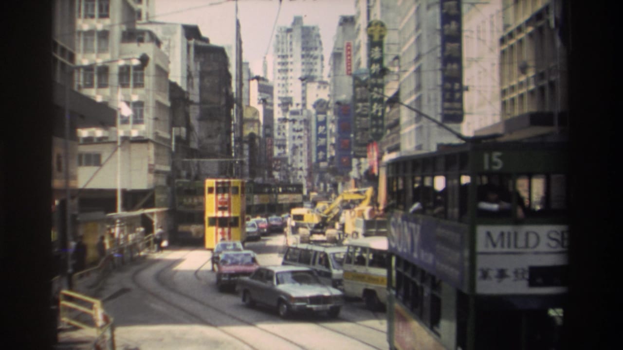 Street traffic with a yellow tram, green tram, cars, a van, and high-rise buildings with signs.