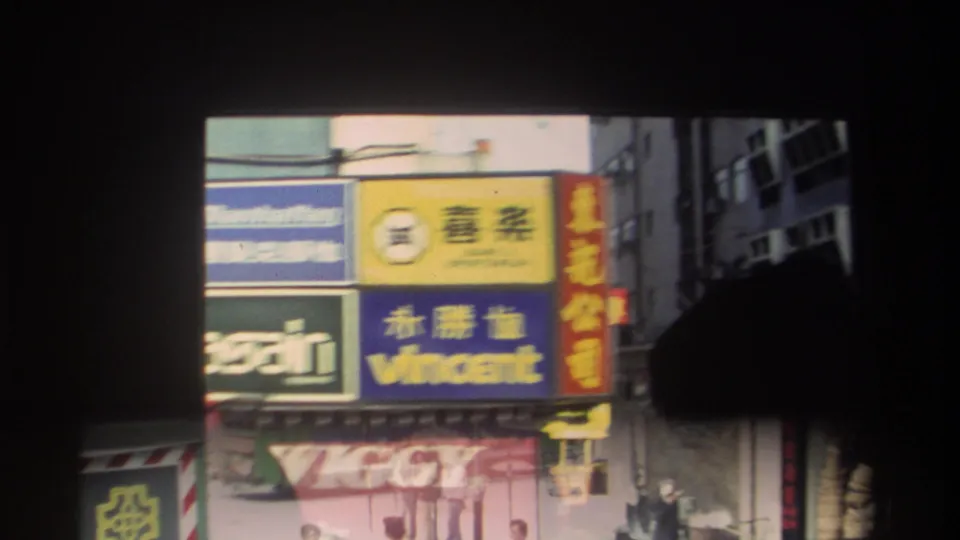 Hong Kong commercial street close-up showing colorful shop signs with Chinese and English text, building facades, and partial traffic below.